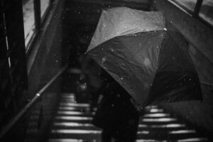 grayscale photography of person holding umbrella on downstair